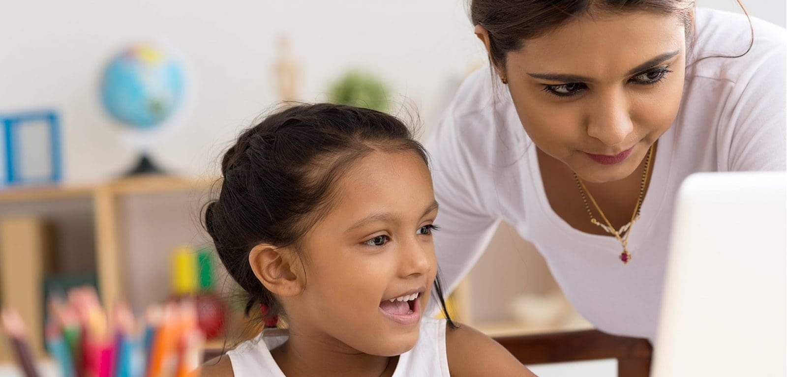 little girl looking at computer in a classroom with her teacher